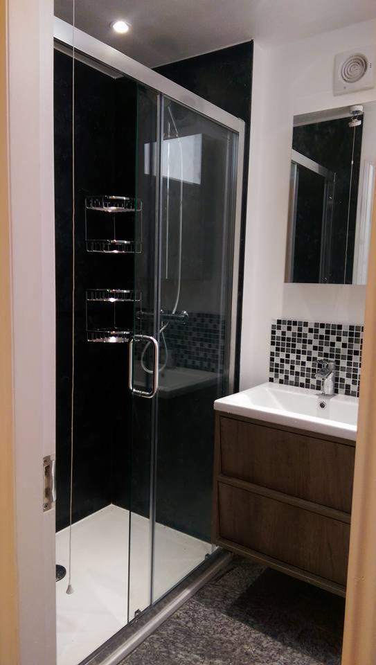 Nowoczesna łazienka z kabiną prysznicową z przesuwnymi drzwiami, umywalką z szafką w kolorze drewna i czarno-białą mozaiką nad umywalką.