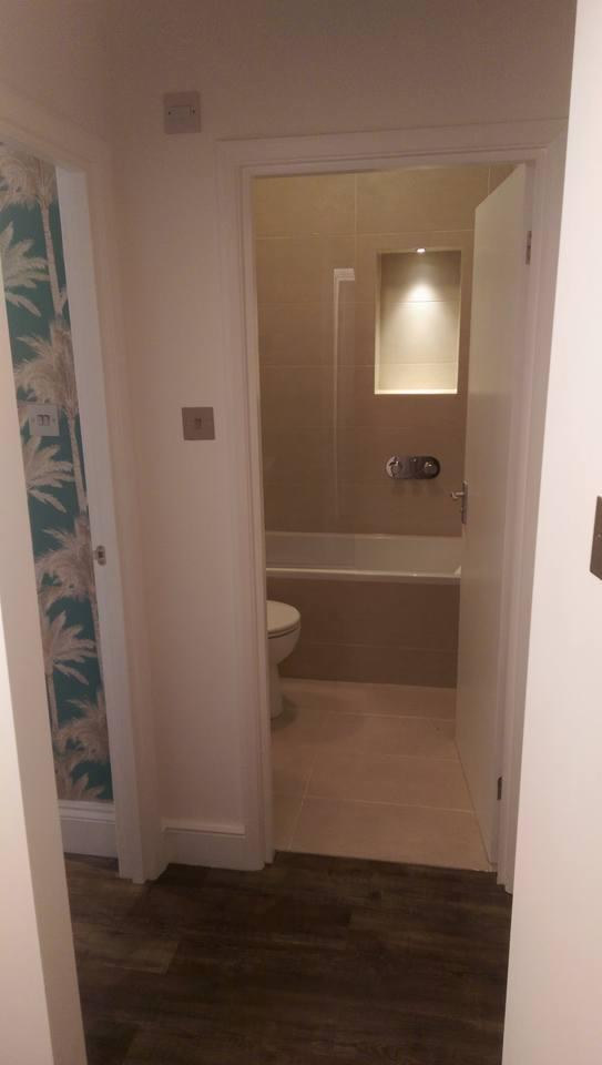 Widok na wyremontowaną łazienkę z toaletą i wanną zza otwartych drzwi, z widoczną ścianą w tropikalne wzory w sąsiednim pomieszczeniu.