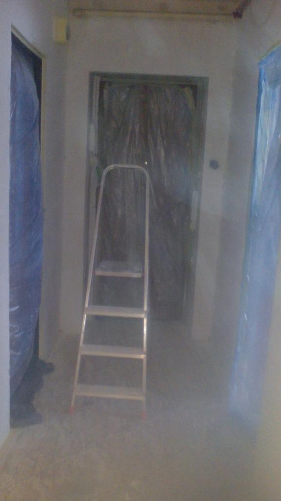 Przygotowanie do malowania mieszkania: pomieszczenie z drabiną i folią ochronną na drzwiach, widoczne ślady po szpachlowaniu na ścianach.