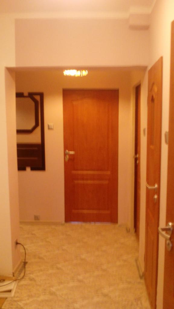 Korytarz po remoncie z trzema drewnianymi drzwiami z srebrnymi klamkami, lustrem w ciemnej ramie i marmurową podłogą w odcieniach beżu.