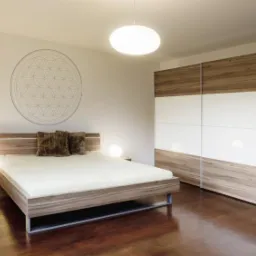 Nowoczesna sypialnia z drewnianą podłogą, ł&oacute;żkiem z drewnianym wezgłowiem, szafkami nocnymi z lampkami, dużą szafą przesuwną z białymi frontami i dekoracją geometryczną na ścianie.