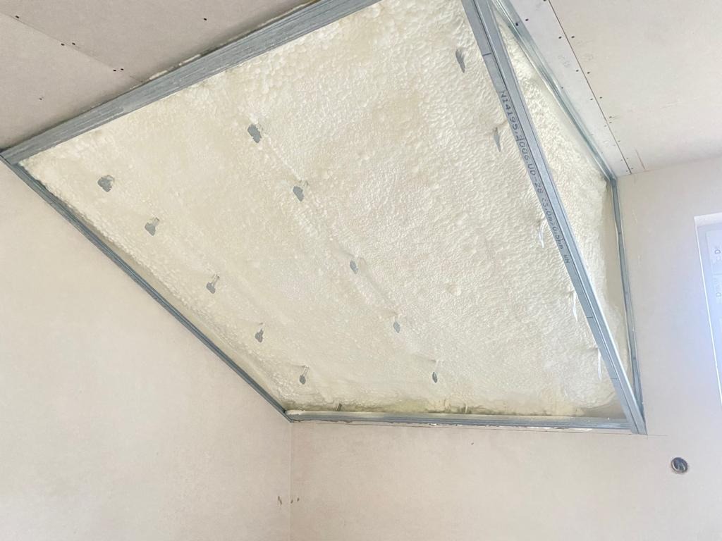 Poddasze z widoczną, jasną pianką PUR między metalowymi profilami, tworzącymi szkielet konstrukcyjny. Widoczne otwory montażowe w piance.