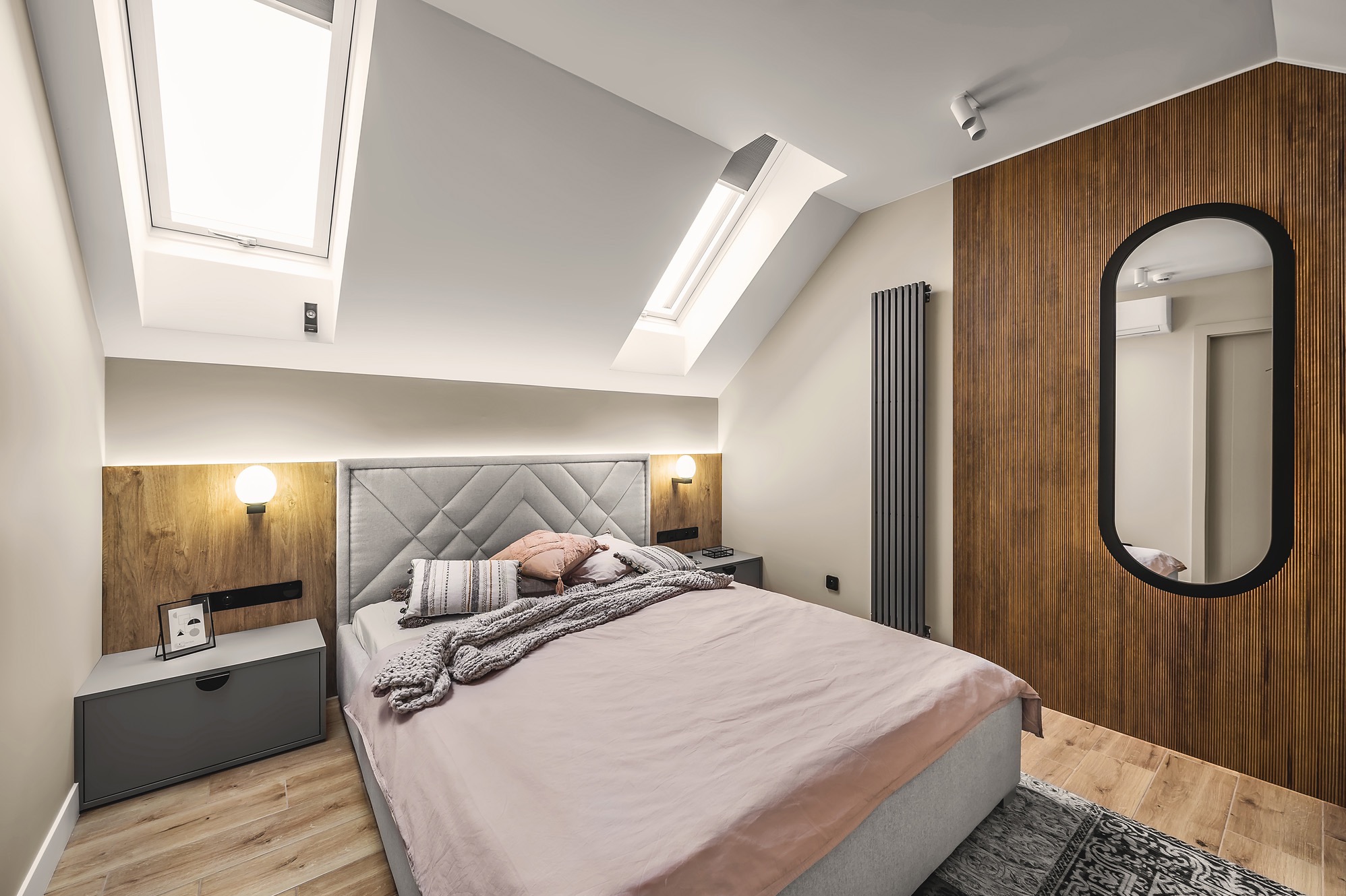 Nowoczesna sypialnia na poddaszu z łóżkiem, drewnianą ścianą z podświetleniem, owalnym lustrem, grzejnikiem panelowym i oknami dachowymi.