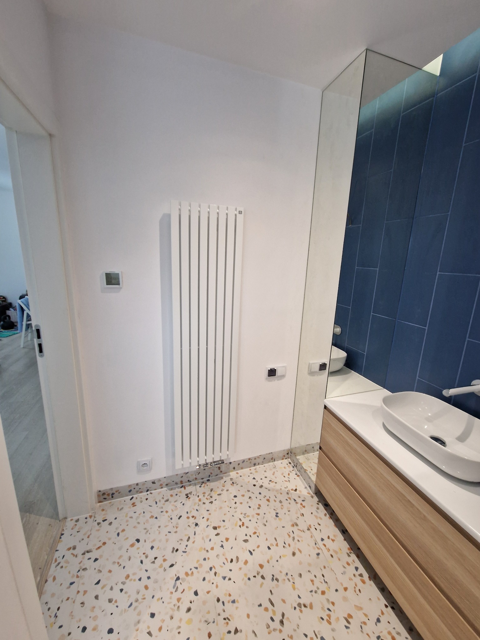 Nowoczesna łazienka z podłogą w stylu terrazzo, białym grzejnikiem panelowym, lustrem i umywalką nablatową, wykończona ciemnoniebieskimi płytkami.