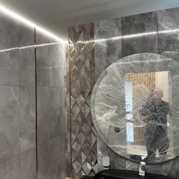 Stet-Tech - Nowoczesna łazienka z szarymi płytkami imitującymi marmur, podświetleniem LED, dekoracyjnym panelem z geometrycznym wzorem i okrągłym lustrem zabezpieczonym folią ochronną przed zabrudzeniem...