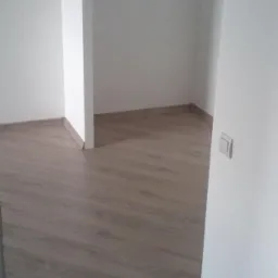 Nowo ułożone panele podłogowe w pustym pokoju w Gdańsku, widoczny fragment ściany z włącznikiem światła.