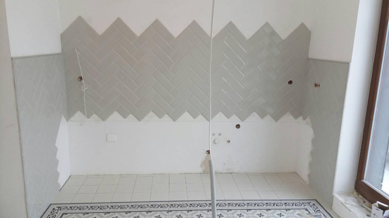 Ściana w trakcie układania płytek w jodełkę, widoczne otwory pod instalacje, częściowo wykończona ściana i podłoga z dekoracyjnym wzorem.