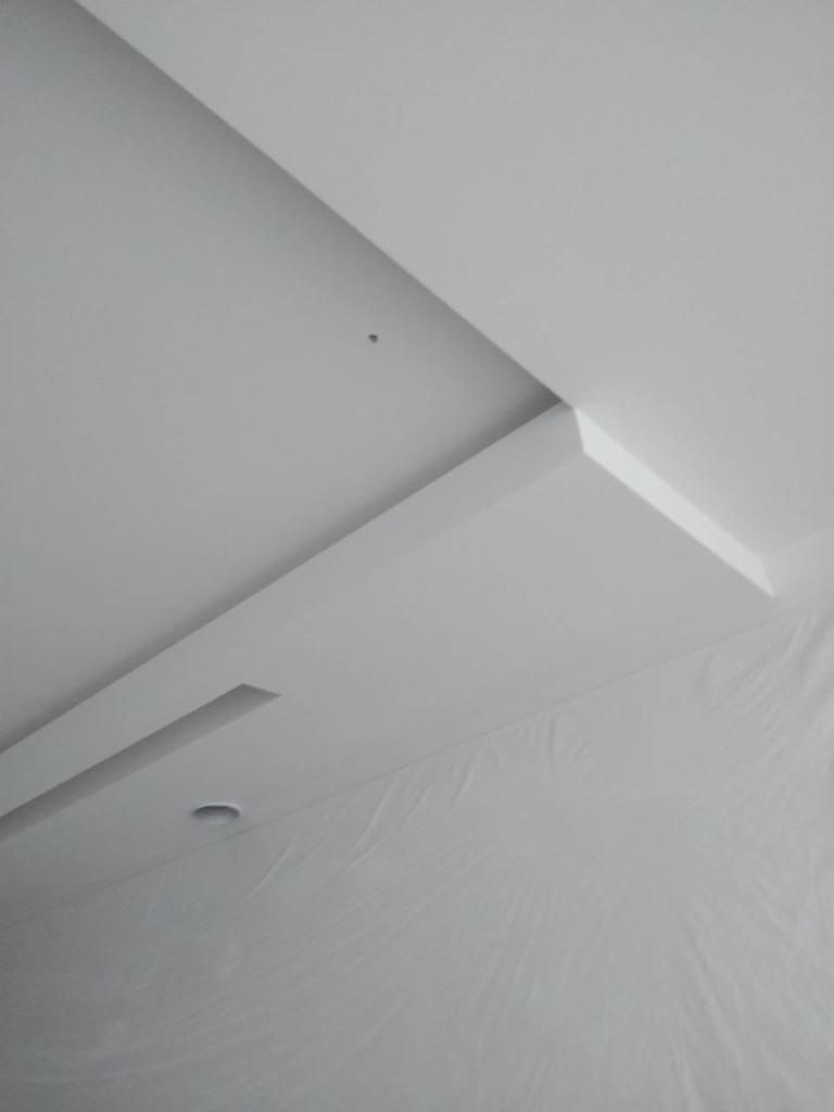 Nowoczesny sufit podwieszany z oświetleniem punktowym i dekoracyjnymi listwami, zabezpieczony folią malarską.