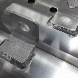 Spoina na elemencie konstrukcyjnym z uchwytem, widoczne charakterystyczne ślady po spawaniu TIG, biały osad w miejscu łączenia.