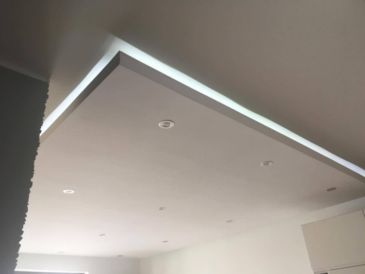 Podwieszany sufit z oświetleniem LED i punktowymi lampami w nowocześnie wykończonym wnętrzu.