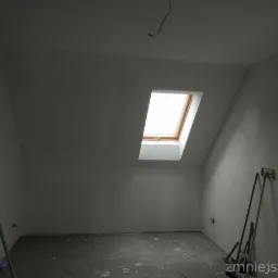 Poddasze po nałożeniu gładzi, widoczne narzędzia malarskie i szpachlarskie, okno dachowe i surowa podłoga.