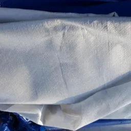 Biała tkanina techniczna złożona na niebieskiej plandece, widoczne faktura materiału i załamania światła.