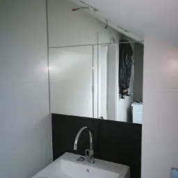 Nowoczesna łazienka z białą umywalką i chromowaną baterią, odbicie w lustrze ukazuje fragment instalacji wodnej w pomieszczeniu obok.