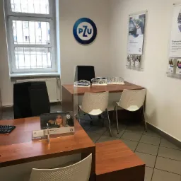 Wnętrze biura ubezpieczeniowego z logo PZU, biurkami, krzesłami i materiałami informacyjnymi na ścianach