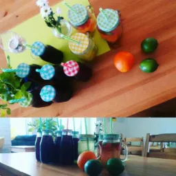 Stół z różnymi napojami w szklanych butelkach i słoikach z kolorowymi pokrywkami i słomkami, pomarańcze i limonki, kwiaty w wazonie.