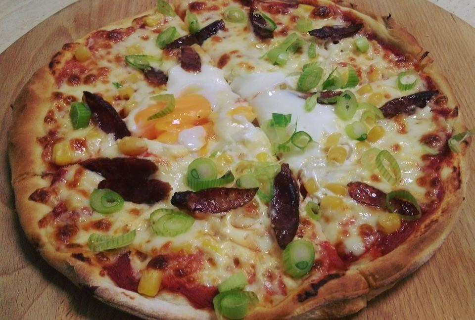 Pizza z jajkiem sadzonym, kukurydzą, zielonym szczypiorkiem i kawałkami mięsa na drewnianej desce.