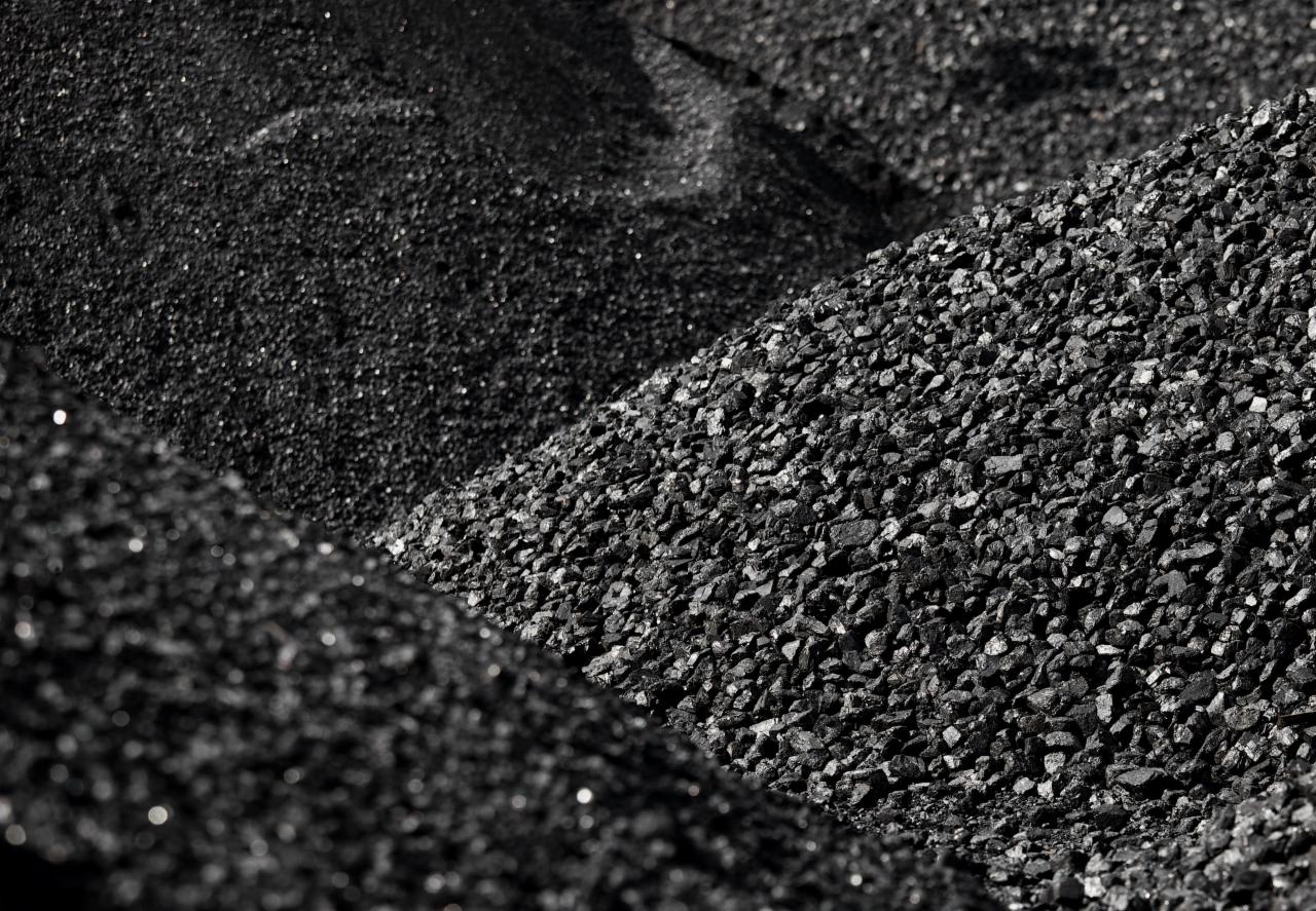Góra czarnego węgla o różnej granulacji, z widocznymi błyszczącymi drobinkami, ułożona w trzy kopce z wyraźnym podziałem na frakcje.
