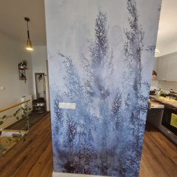 MJP Mateusz Wolny - Ściana z fototapetą przedstawiającą motyw lasu bambusowego w odcieniach szarości i błękitu, widoczne włączniki światła, fragment schodów z drewnianymi stopniami i metalową barierką oraz kuchnia w tle.