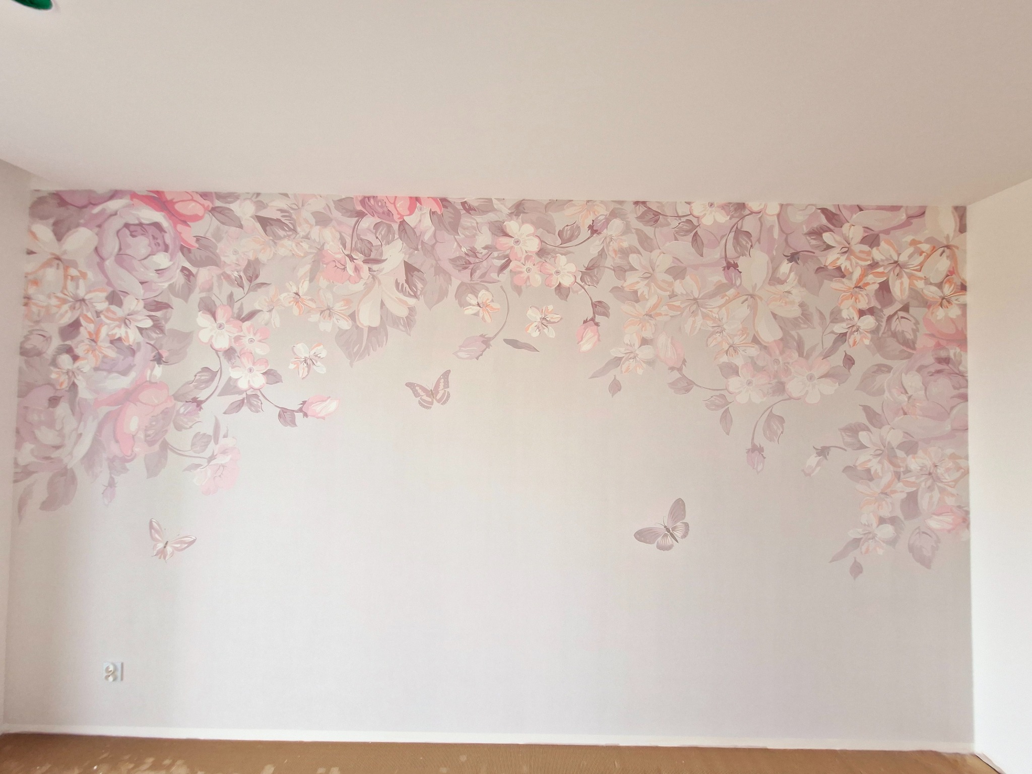 Ściana po położeniu tapety w pastelowe kwiaty i motyle. Dekoracja wnętrza pokoju z widocznym gniazdkiem elektrycznym w dolnej części ściany.