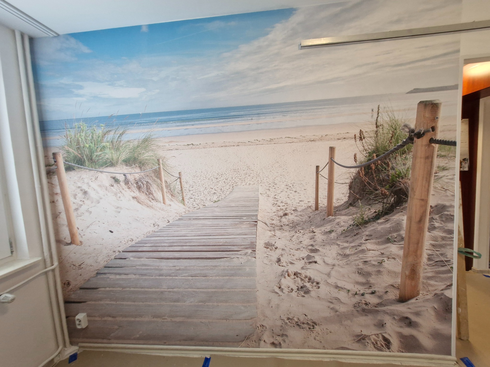 Fototapeta na ścianie: plaża z drewnianą ścieżką i błękitnym niebem, tworząca iluzję przestrzeni. Realizacja z dbałością o detale i spójność wzoru na całej powierzchni.