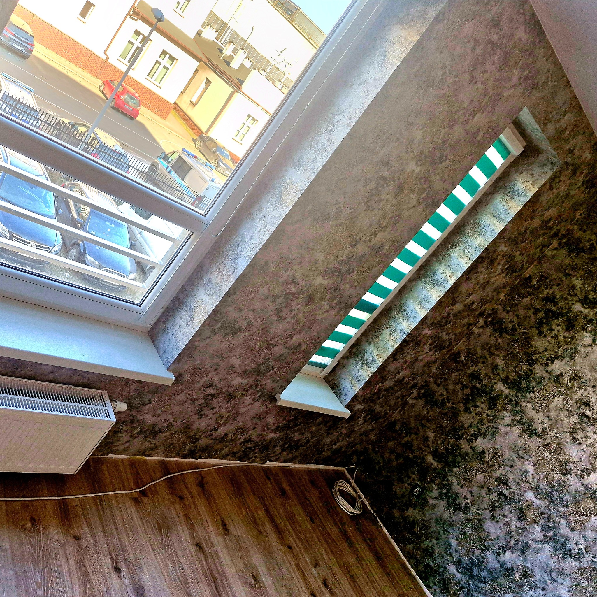 Ściana po renowacji z dekoracyjną strukturą, widok z dołu, okno dachowe z żaluzjami, grzejnik. Wyraźna faktura ściany, widoczne detale wykończenia.