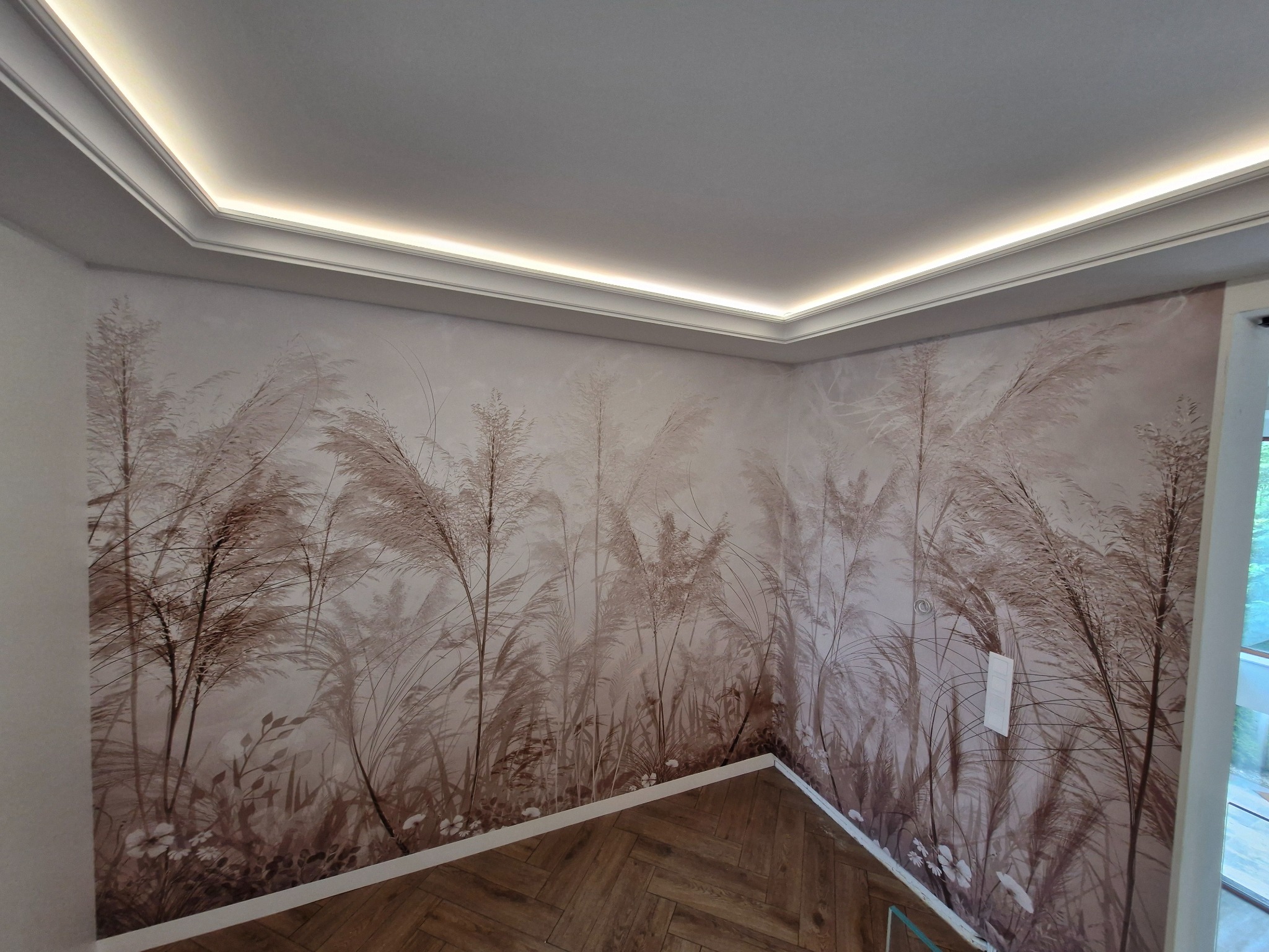 Pokój po remoncie: ściany z tapetą w motywy roślinne, listwa oświetleniowa pod sufitem i parkiet ułożony w jodełkę francuską. Subtelne, stonowane barwy.