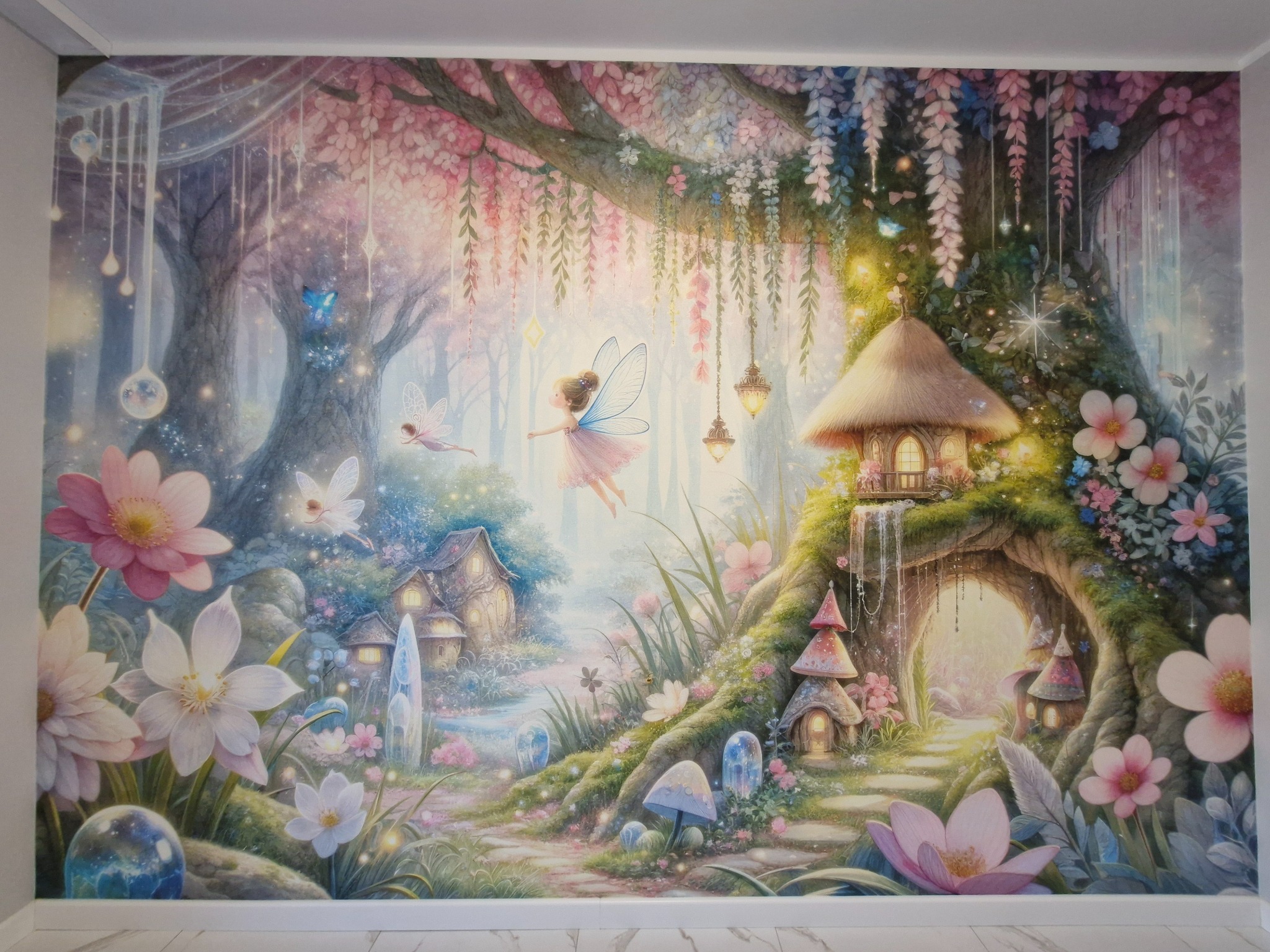 Tapeta ścienna z motywem baśniowego lasu, z wróżkami, kwiatami i domkami, w pastelowych odcieniach różu, fioletu i zieleni. Realizacja tapetowania.