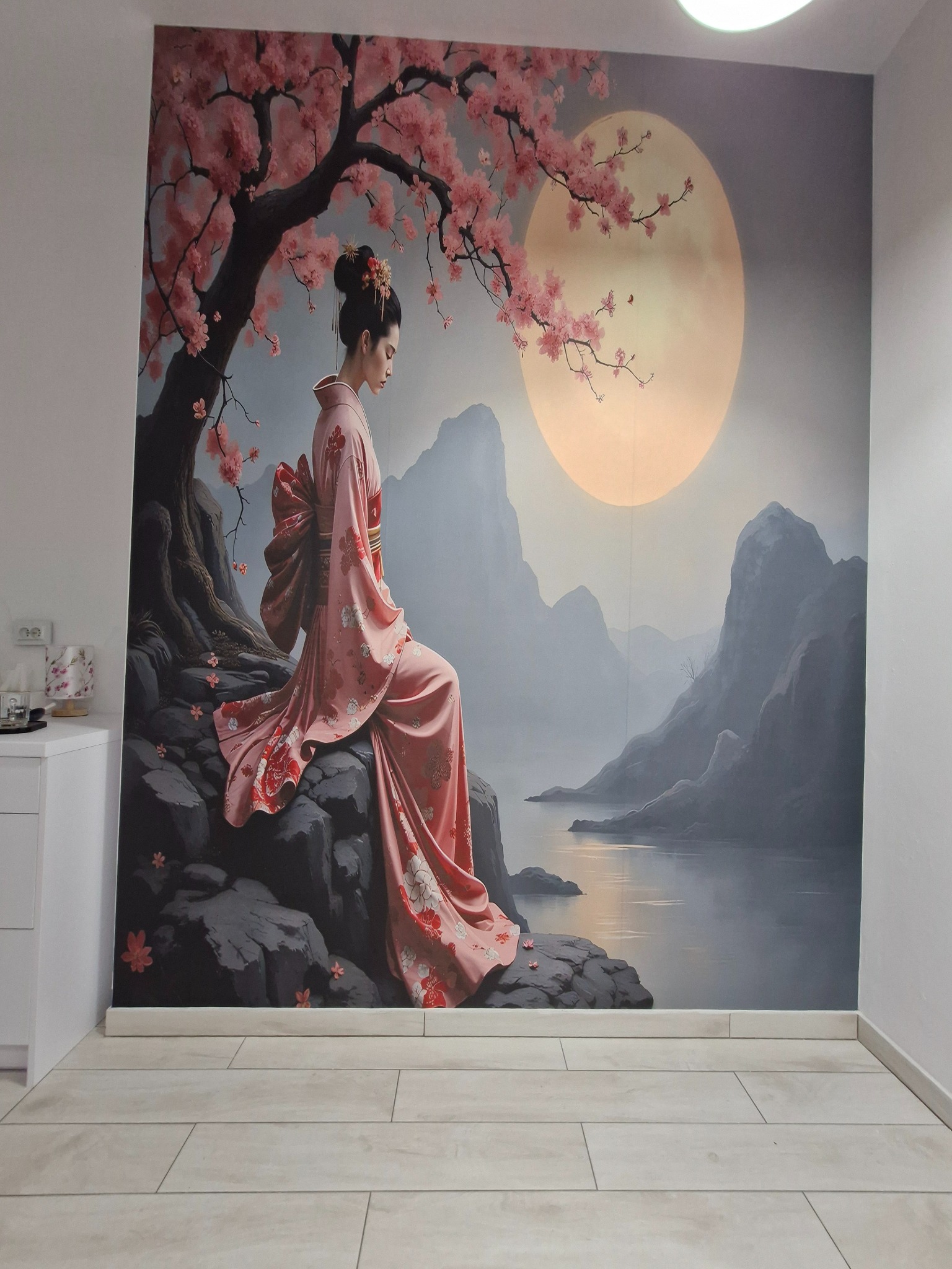 Fototapeta z motywem gejszy w kimonie na tle księżyca i gór, z kwitnącą wiśnią. Realizacja z dbałością o detale, tworząca unikalny klimat w pomieszczeniu.