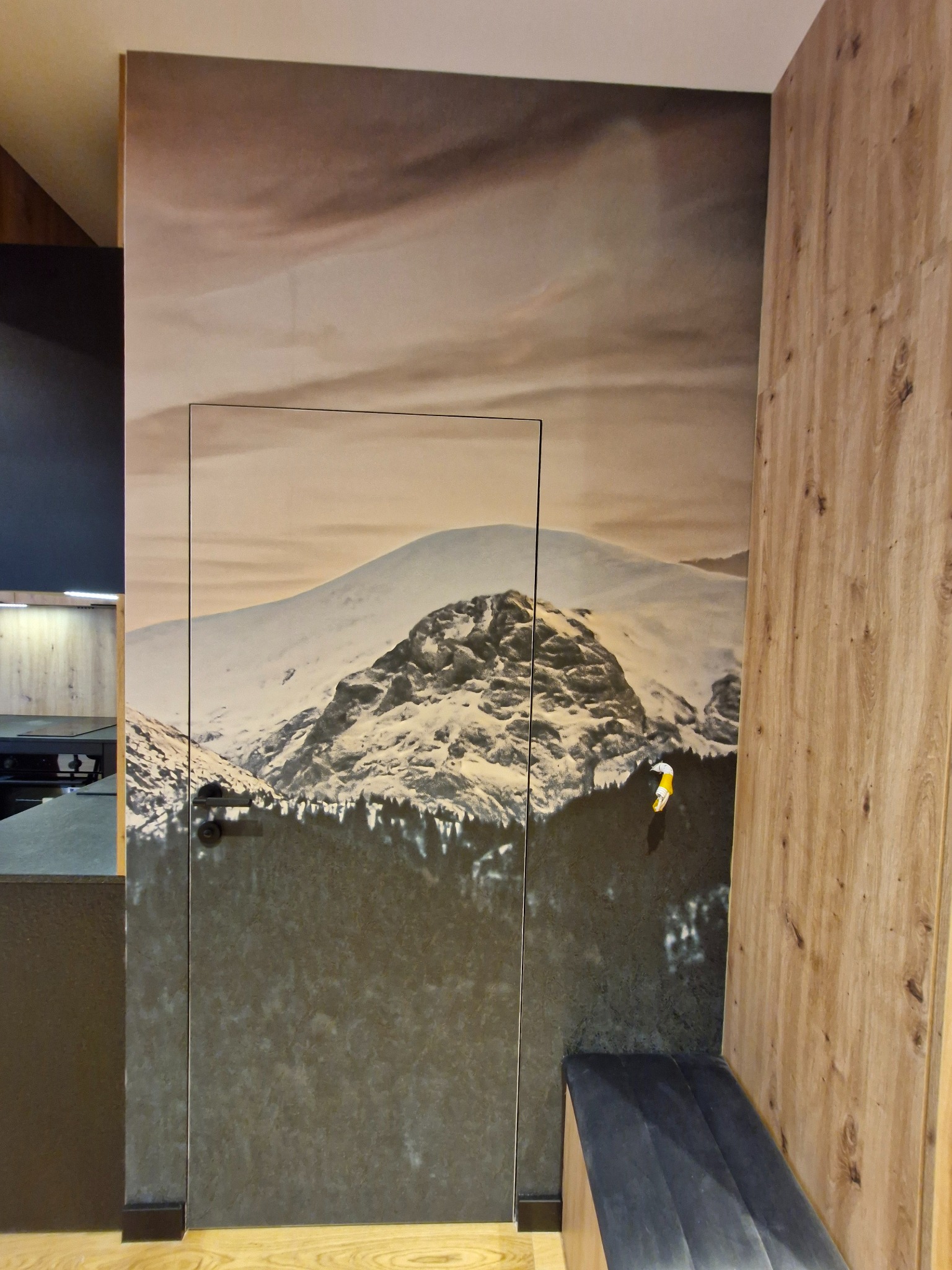 Tapeta z motywem górskim na ścianie z ukrytymi drzwiami, obok drewniana boazeria. Nowoczesne wykończenie wnętrza z akcentem natury i ukrytych rozwiązań.