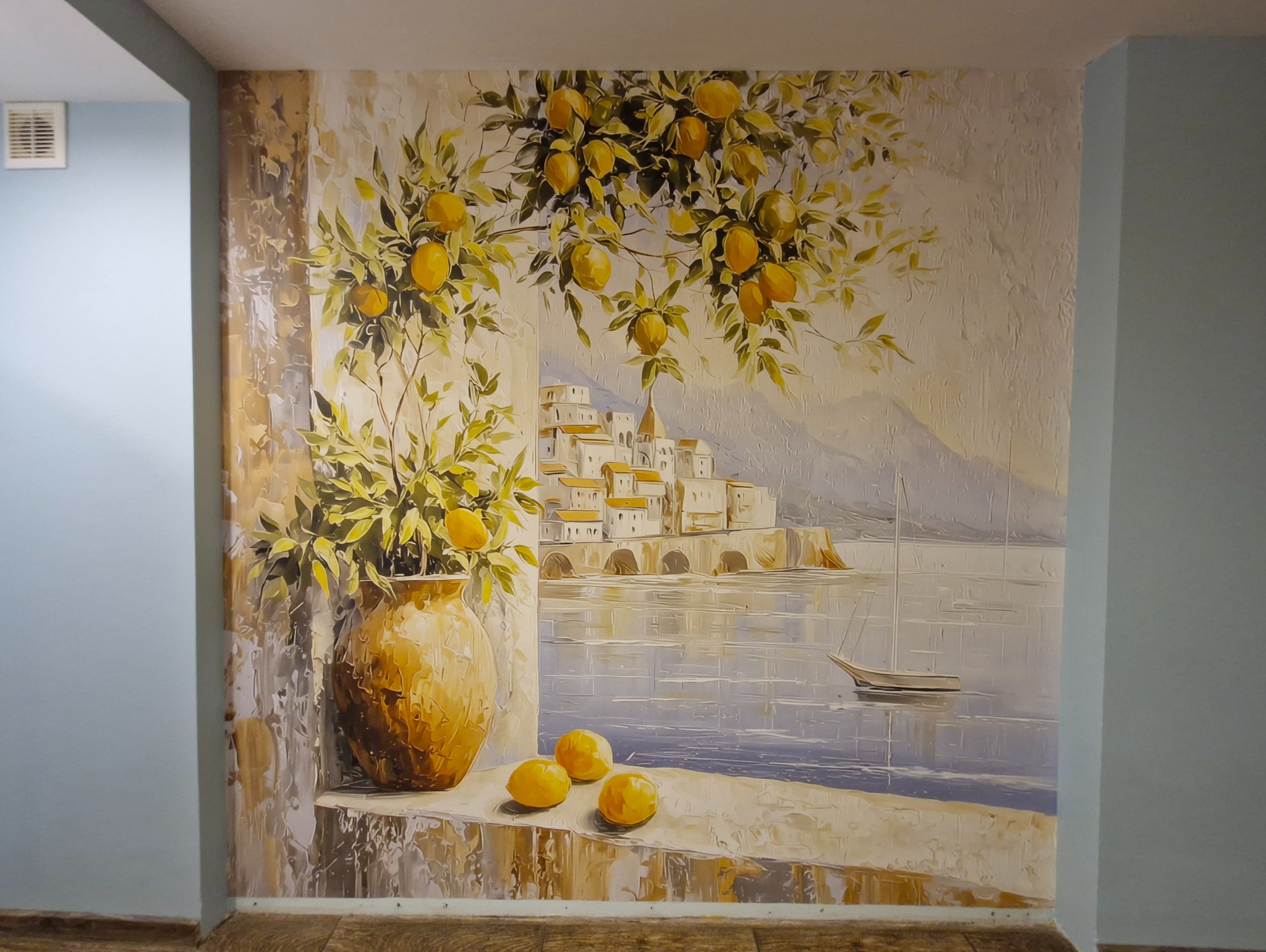 Ręcznie malowana ściana z motywem cytryn, wazonu i pejzażu nadmorskiego. Tekstura farby tworzy efekt trójwymiarowości. Dekoracja wnętrza w stylu śródziemnomorskim.