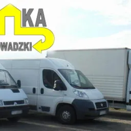 Trzy białe busy transportowe różnych marek stojące obok siebie, z logiem firmy na pierwszym planie z napisem 'EMKA Przeprowadzki' i strzałkami.
