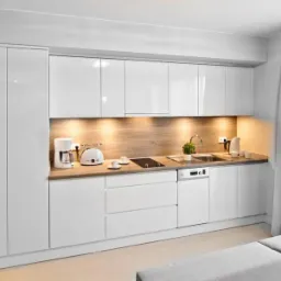 Nowoczesna, biała kuchnia z połyskiem, drewnopodobny blat, oświetlenie podszafkowe, ekspres do kawy i toster na blacie, minimalistyczny wystrój, jasne wnętrze.