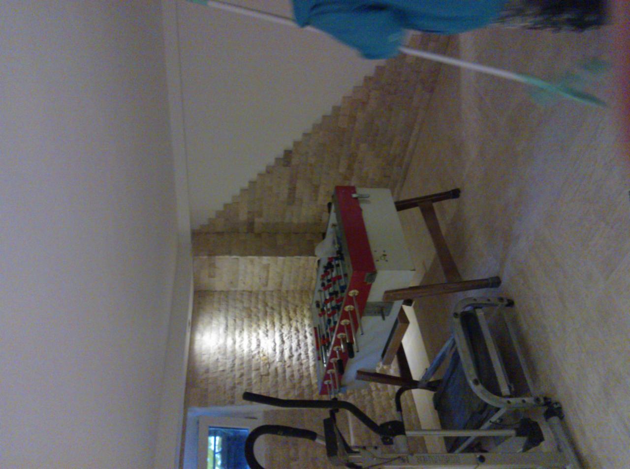 Nierówna ściana z cegły w trakcie prac wykończeniowych, widoczne narzędzia i sprzęt sportowy w pomieszczeniu.