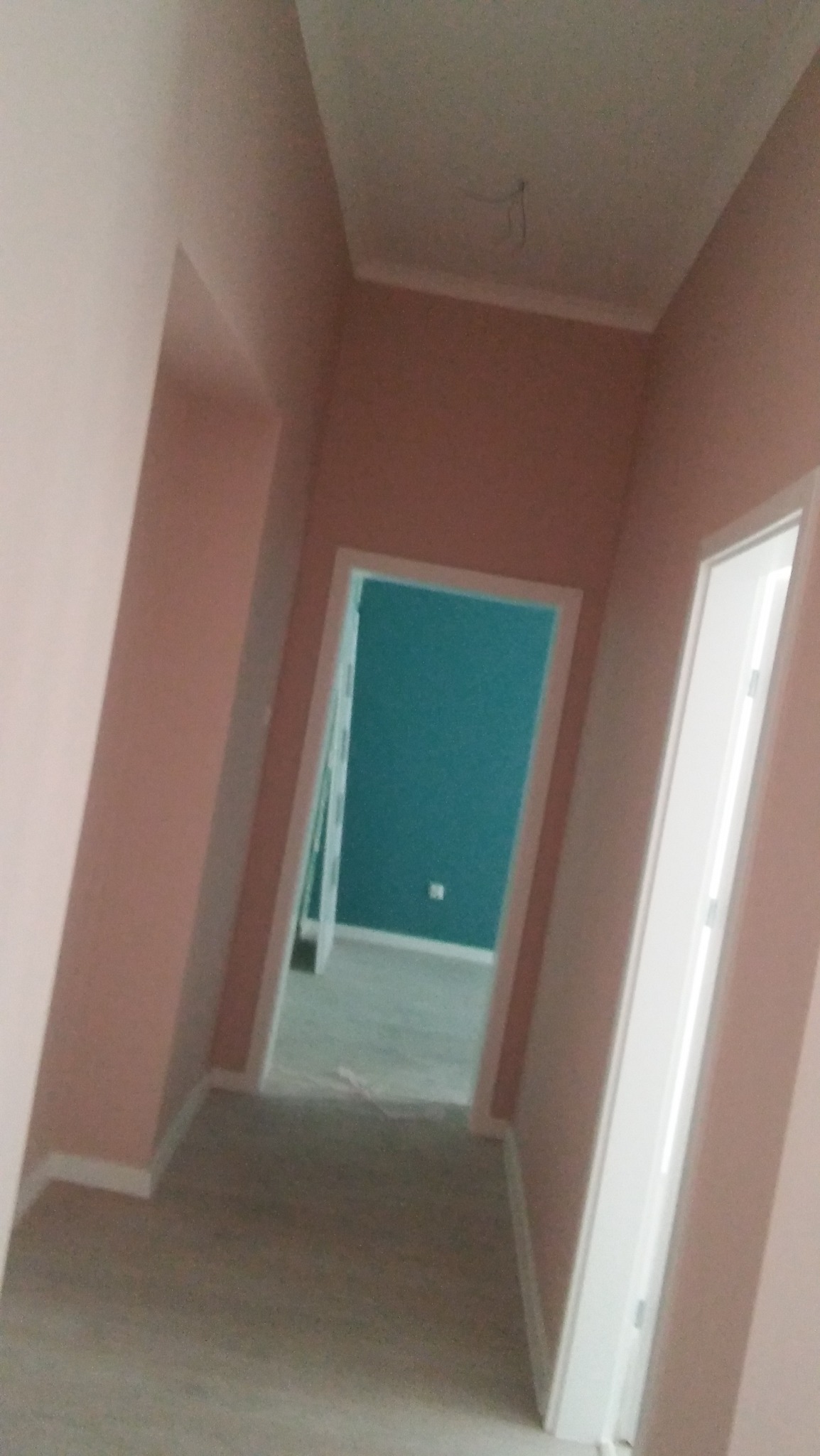 Korytarz po odświeżeniu, ściany pomalowane na pudrowy róż, widoczne białe listwy przypodłogowe i ościeżnice, w tle pokój z turkusową ścianą.