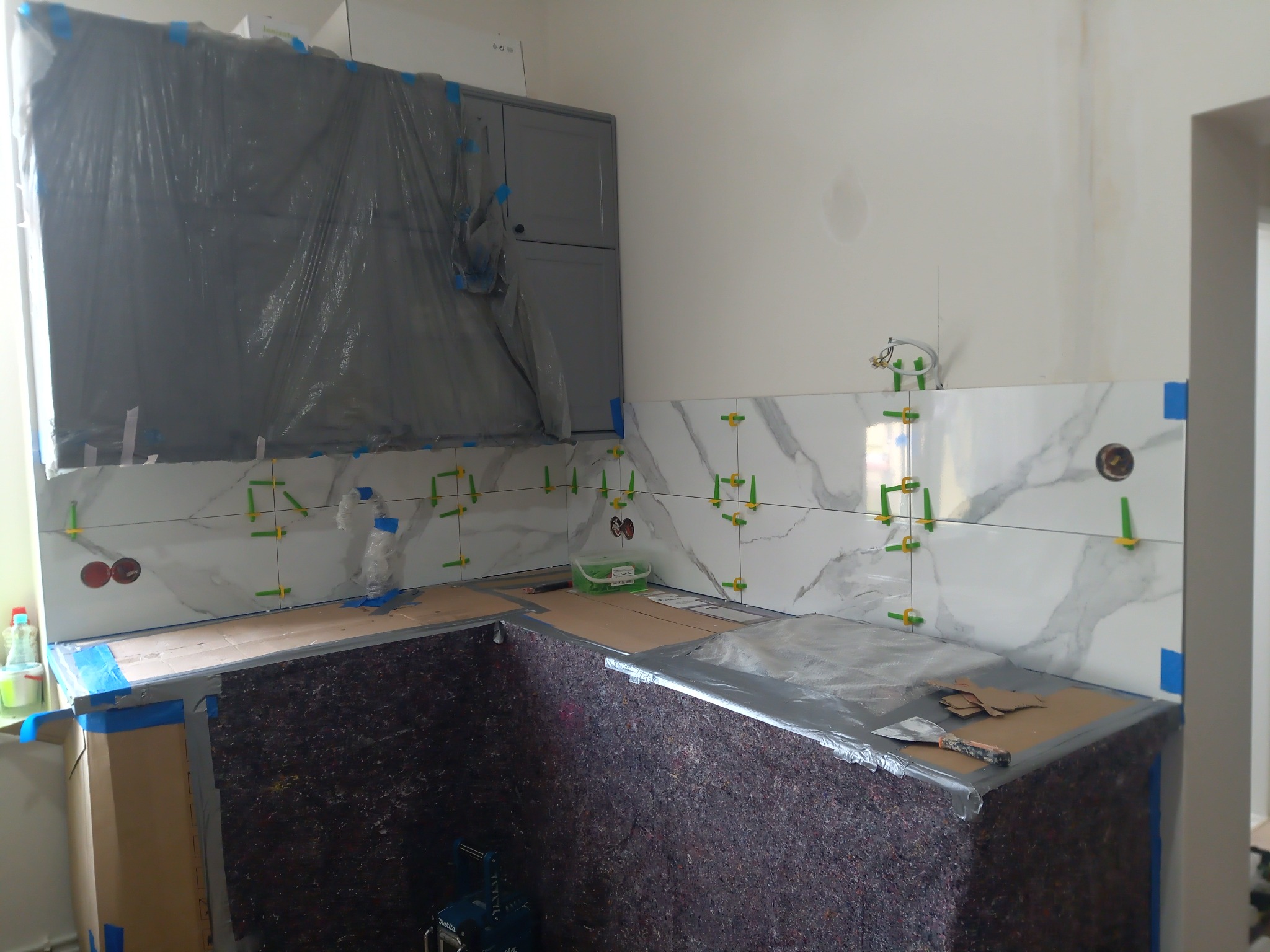 Montaż płytek marmurkowych w kuchni w Inowrocławiu, widoczne plastikowe krzyżyki dystansowe, zabezpieczone folią meble i blaty robocze w trakcie prac.