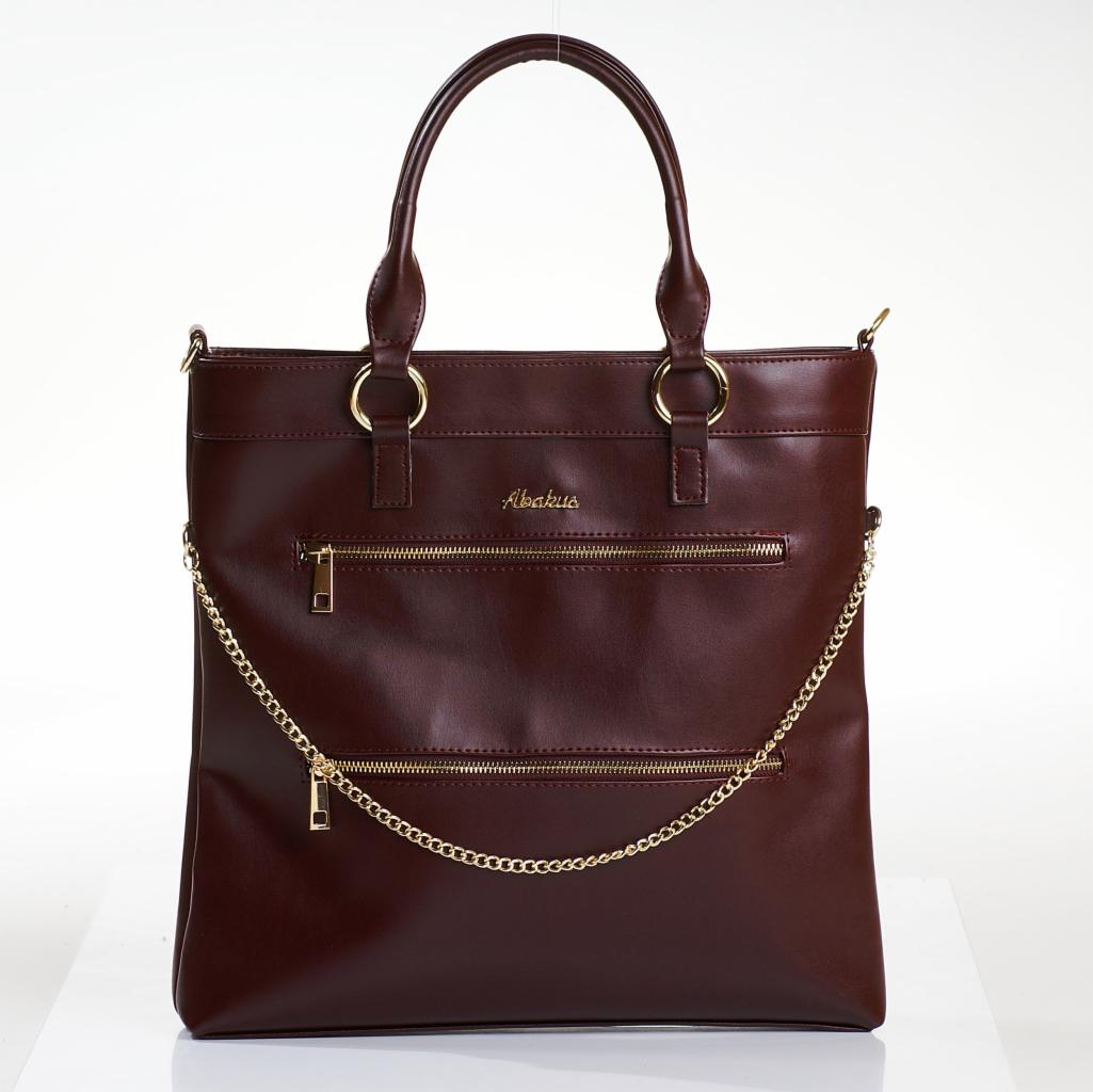 Burgundowa torba shopper z dwoma złotymi zamkami błyskawicznymi i łańcuszkiem, widoczne uchwyty i złote okucia, na jasnym tle.