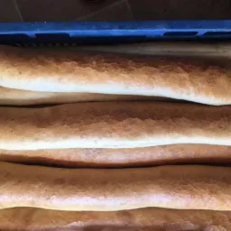 Świeżo upieczone, rumiane bagietki ułożone w niebieskiej skrzynce, widoczne delikatne pęknięcia na skórce.