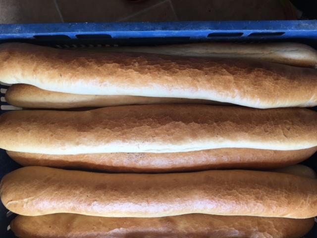 Świeżo upieczone, rumiane bagietki ułożone w niebieskiej skrzynce, widoczne delikatne pęknięcia na skórce.