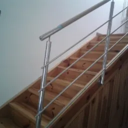 Schody drewniane z metalową balustradą ze stali nierdzewnej, zabezpieczoną kartonem na górnej poręczy, widok z dołu.