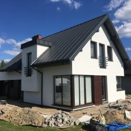 Zakład Ogólnobudowlany ZEN- BUD Zenon Kuźnik - Nowoczesny dom jednorodzinny z białą elewacją i grafitowym dachem, widoczny w trakcie prac wykończeniowych wokół budynku, z hałdą ziemi i gruzu na trawniku.