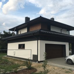 Zakład Ogólnobudowlany ZEN- BUD Zenon Kuźnik - Nowoczesny dom jednorodzinny z białą elewacją, ciemnym dachem i drewnianymi akcentami, widoczny z boku, z samochodem zaparkowanym na podjeździe.