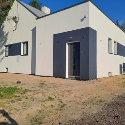 Zakład Ogólnobudowlany ZEN- BUD Zenon Kuźnik - Nowoczesny dom jednorodzinny z biało-szarą elewacją, ciemnymi akcentami wokół okien i drzwi, widoczne pozostałości po pracach budowlanych na gruncie.