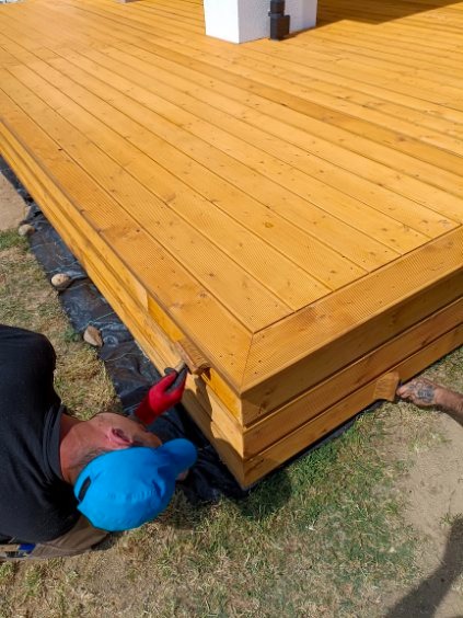 Montaż drewnianego tarasu w Kaliskach. Widoczny fragment gotowego tarasu z desek i pracownik w trakcie wykończenia krawędzi. Elementy zaimpregnowane.