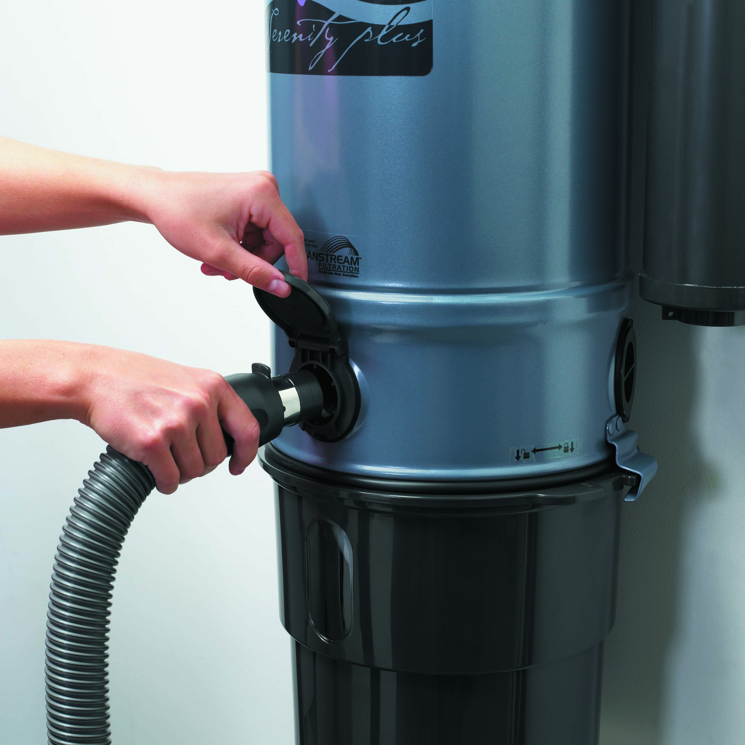 Podłączenie węża do gniazda centralnego odkurzacza 'Serenity Plus' z otwartą klapką, widoczny zbiornik na kurz i naklejka 'VANSTREAM FILTRATION'.