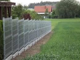 Nowoczesne, panelowe ogrodzenie z metalową siatką, zamontowane na betonowej podmurówce w Nysie. Widok z zewnątrz posesji na tle zielonego trawnika i drzew.