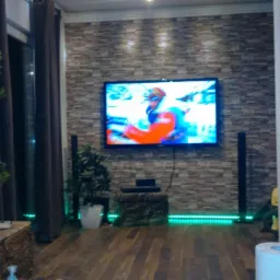 Salon z panelami ściennymi imitującymi cegłę, telewizorem, drewnianą podłogą, kominkiem i dekoracyjnym oświetleniem LED.