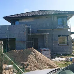 Budowa domu jednorodzinnego w trakcie ocieplania, widoczne rusztowania, bloczki betonu komórkowego, styropian, piasek i materiały budowlane marki Roben.