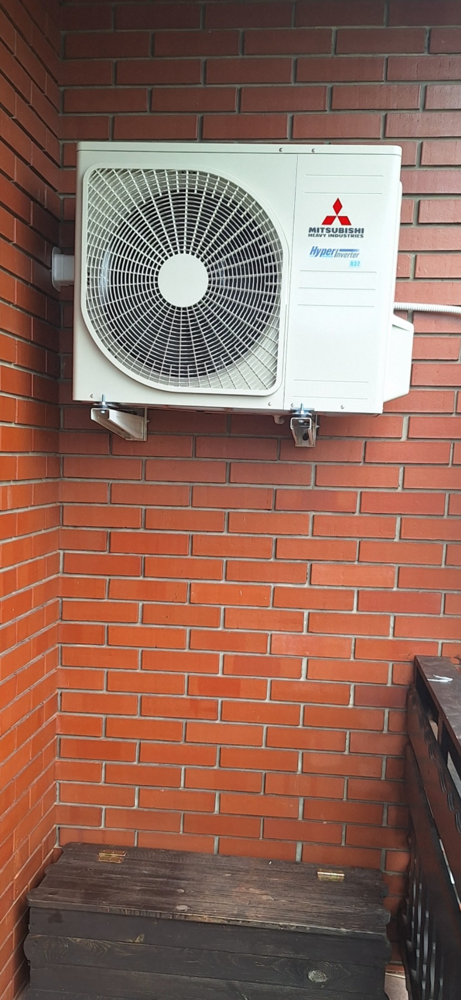 Zewnętrzna jednostka klimatyzacji Mitsubishi Heavy Industries zamontowana na ceglanej ścianie, widoczne metalowe wsporniki i logo firmy.