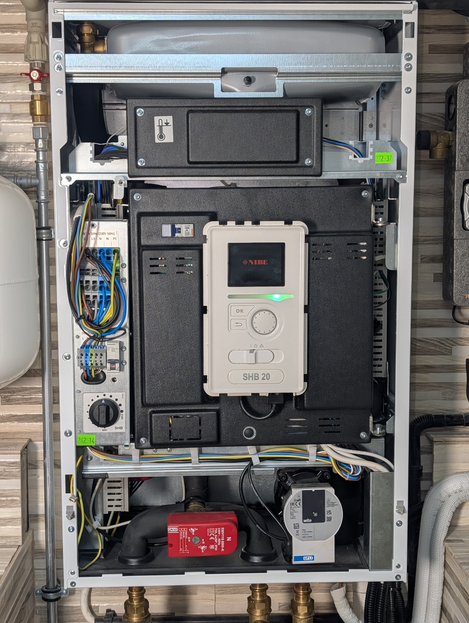 Wnętrze pompy ciepła NIBE SHB 20 z widocznym panelem sterowania, okablowaniem i elementami hydraulicznymi. Detaliczne ujęcie instalacji w obudowie.