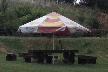 Zadaszone miejsce do siedzenia z drewnianym stołem i ławkami na trawiastym terenie, parasol reklamowy Algida.